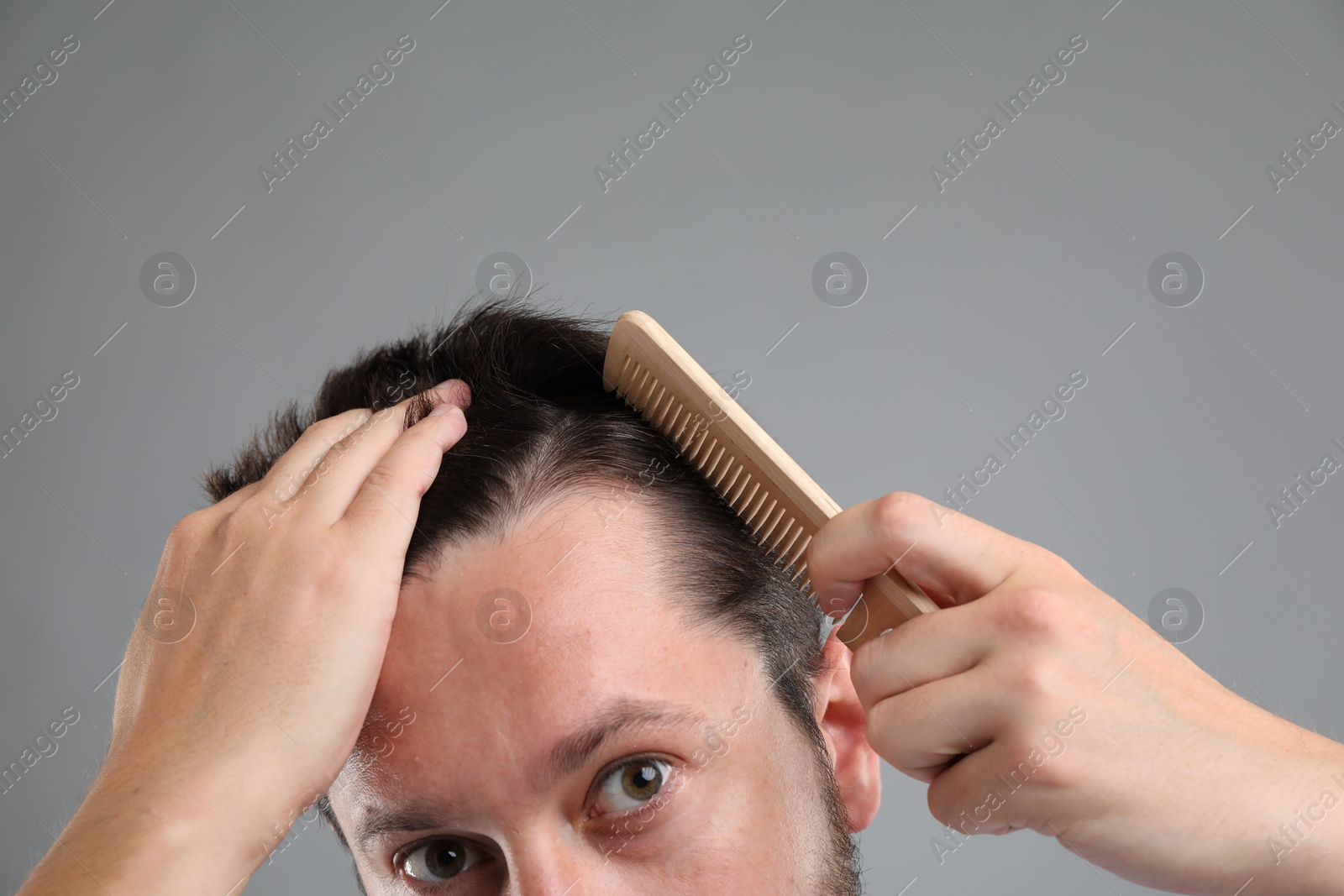 Photo of Man brushing his hair on gray background, closeup. Alopecia problem