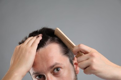 Man brushing his hair on gray background, closeup. Alopecia problem