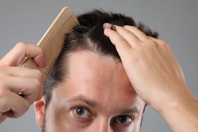 Man brushing his hair on gray background, closeup. Alopecia problem