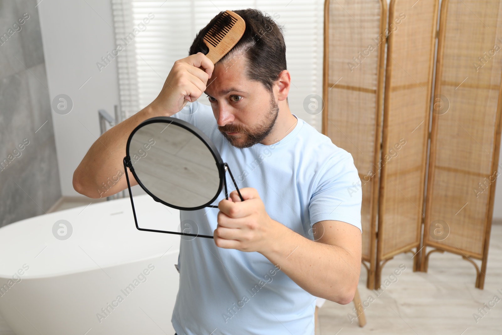 Photo of Man brushing his hair near mirror indoors. Alopecia problem