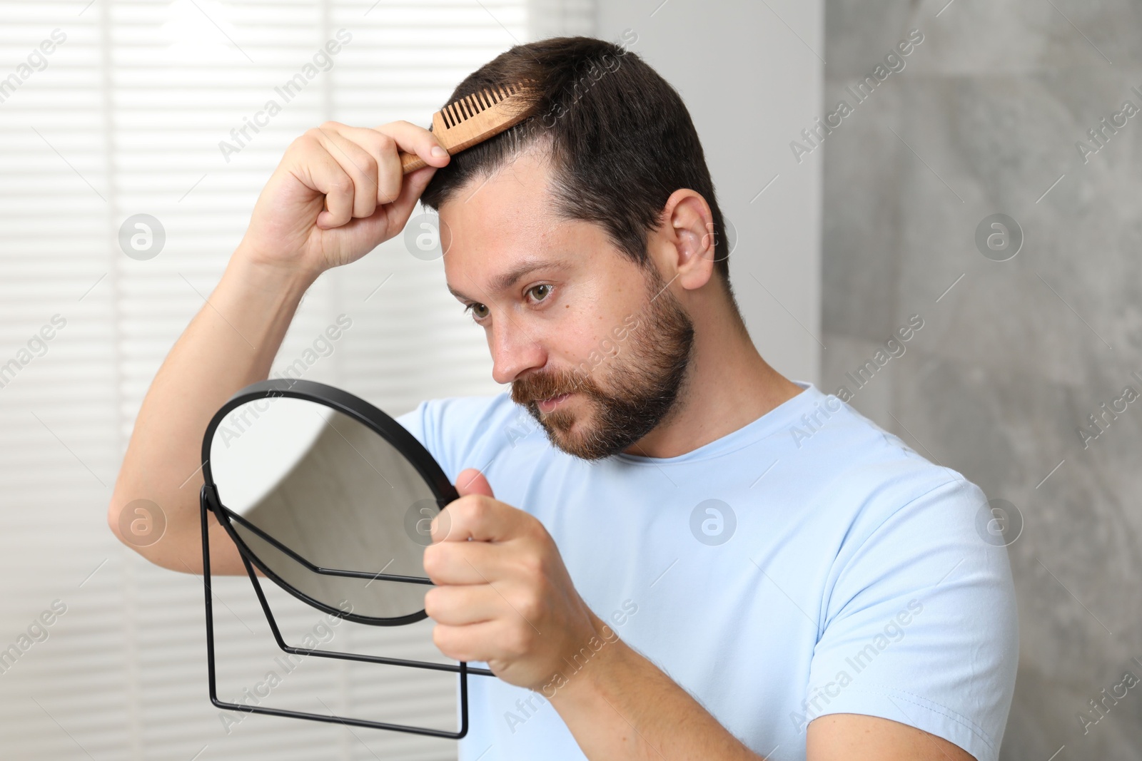 Photo of Man brushing his hair near mirror indoors. Alopecia problem