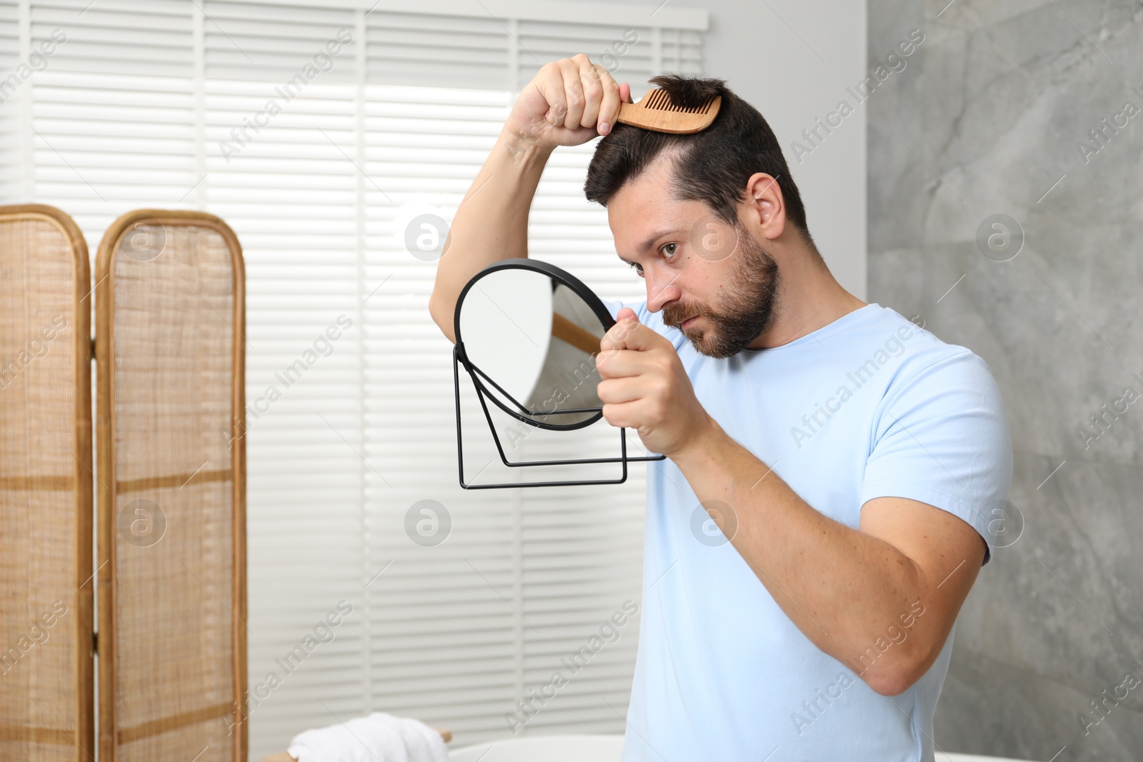 Photo of Man brushing his hair near mirror indoors. Alopecia problem