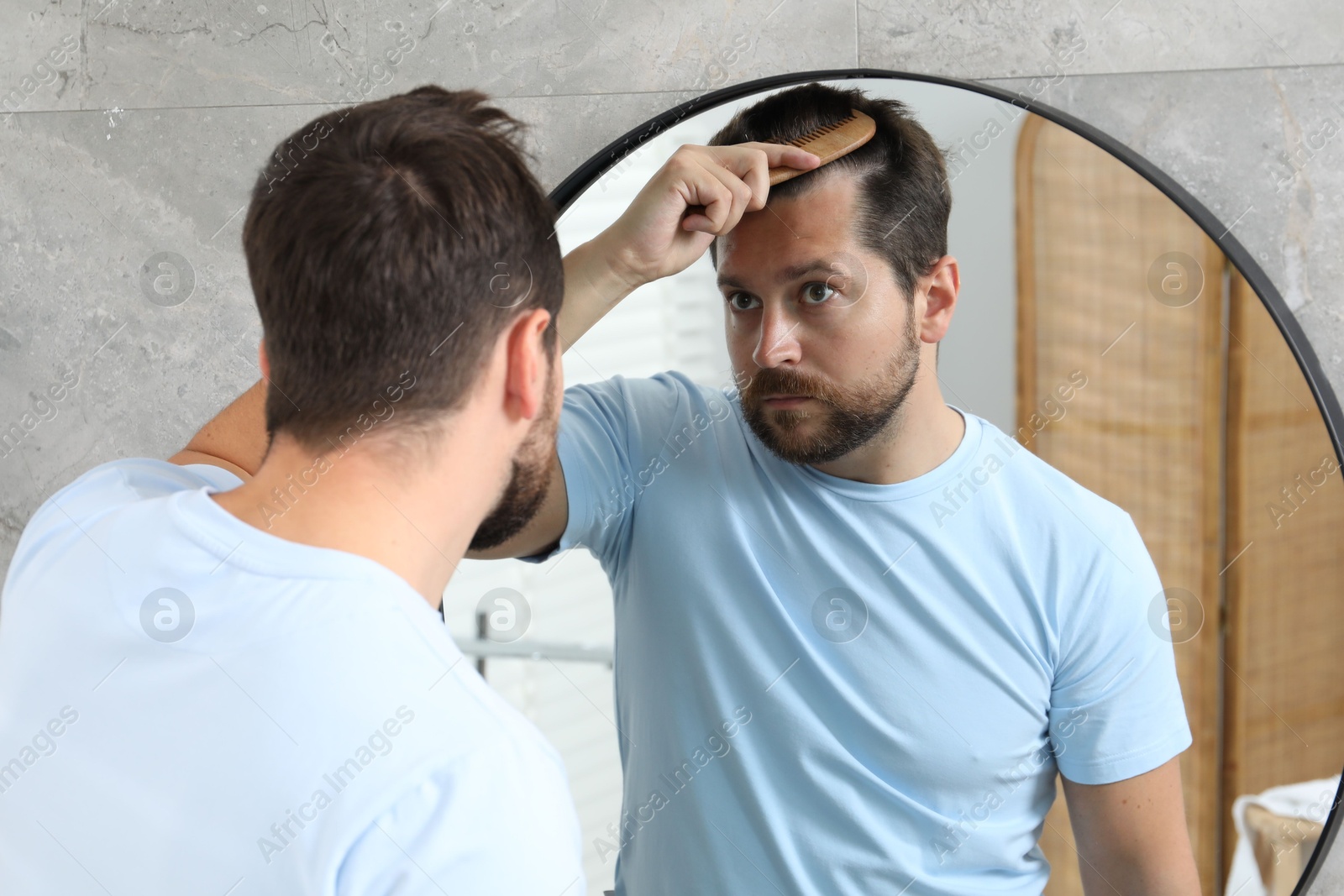 Photo of Man brushing his hair near mirror indoors. Alopecia problem