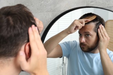 Man brushing his hair near mirror indoors. Alopecia problem