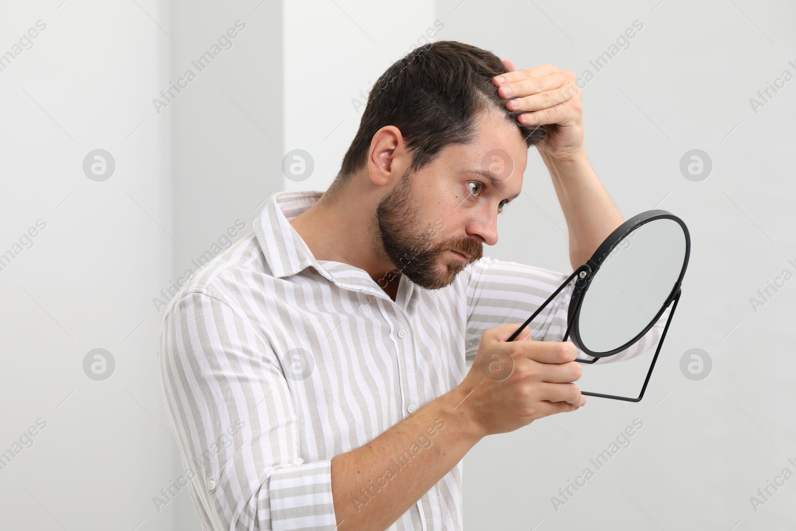 Photo of Man with hair loss problem looking at mirror indoors