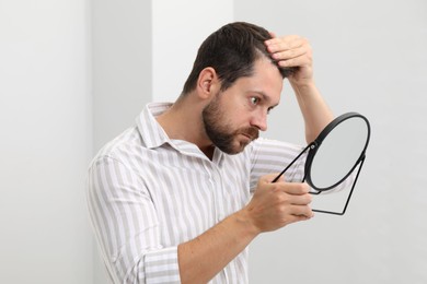 Man with hair loss problem looking at mirror indoors