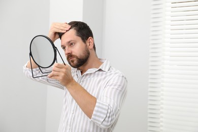 Man with hair loss problem looking at mirror indoors