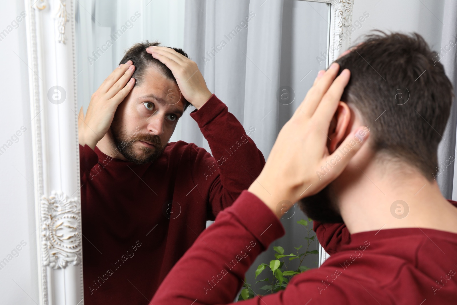 Photo of Man with hair loss problem looking at mirror indoors