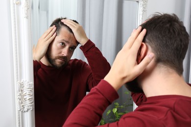 Photo of Man with hair loss problem looking at mirror indoors