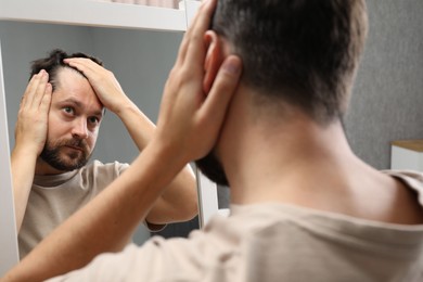 Photo of Man with hair loss problem looking at mirror indoors