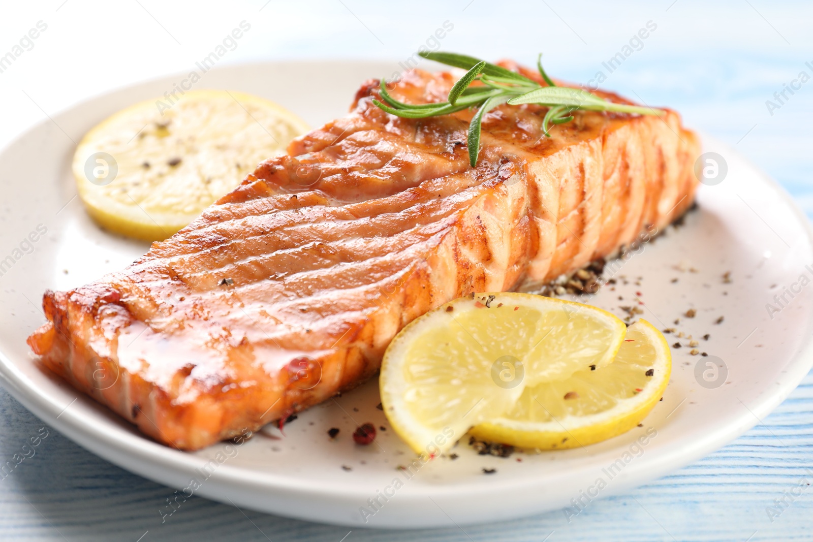 Photo of Delicious grilled salmon fillet served on light blue wooden table, closeup