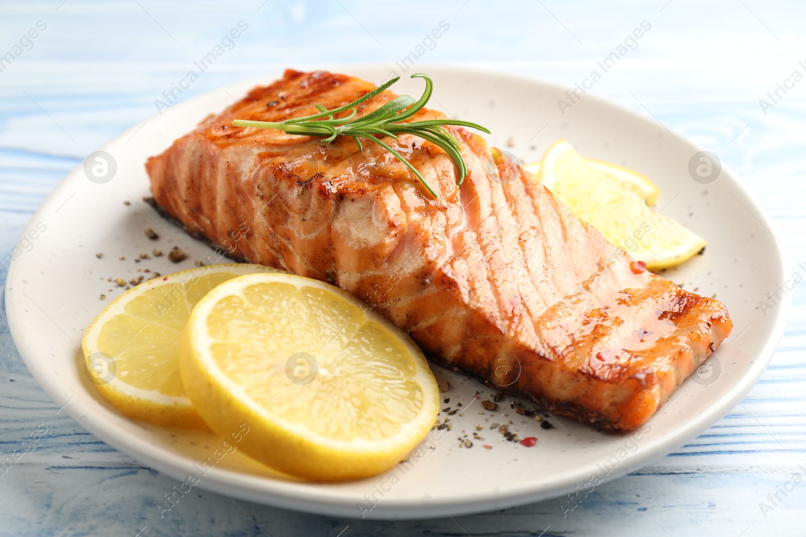 Photo of Delicious grilled salmon fillet served on light blue wooden table, closeup