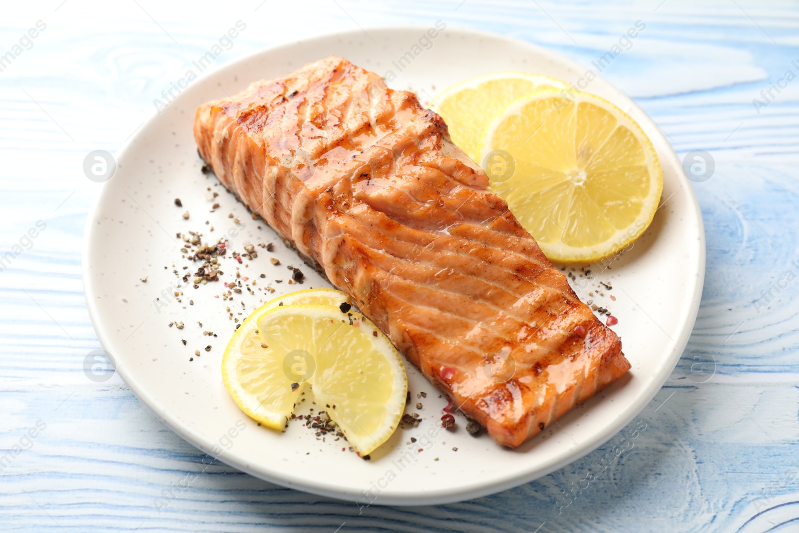 Photo of Delicious grilled salmon fillet served on light blue wooden table, closeup