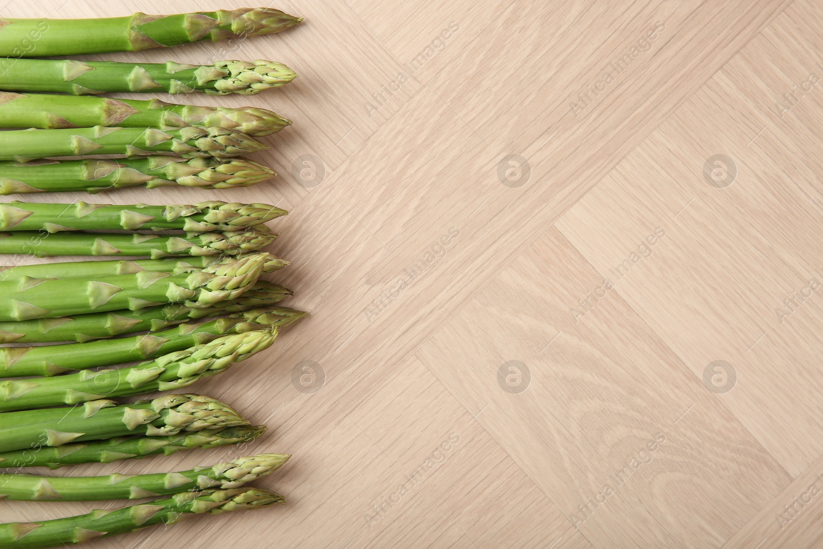 Photo of Fresh green asparagus stems on wooden table, top view. Space for text