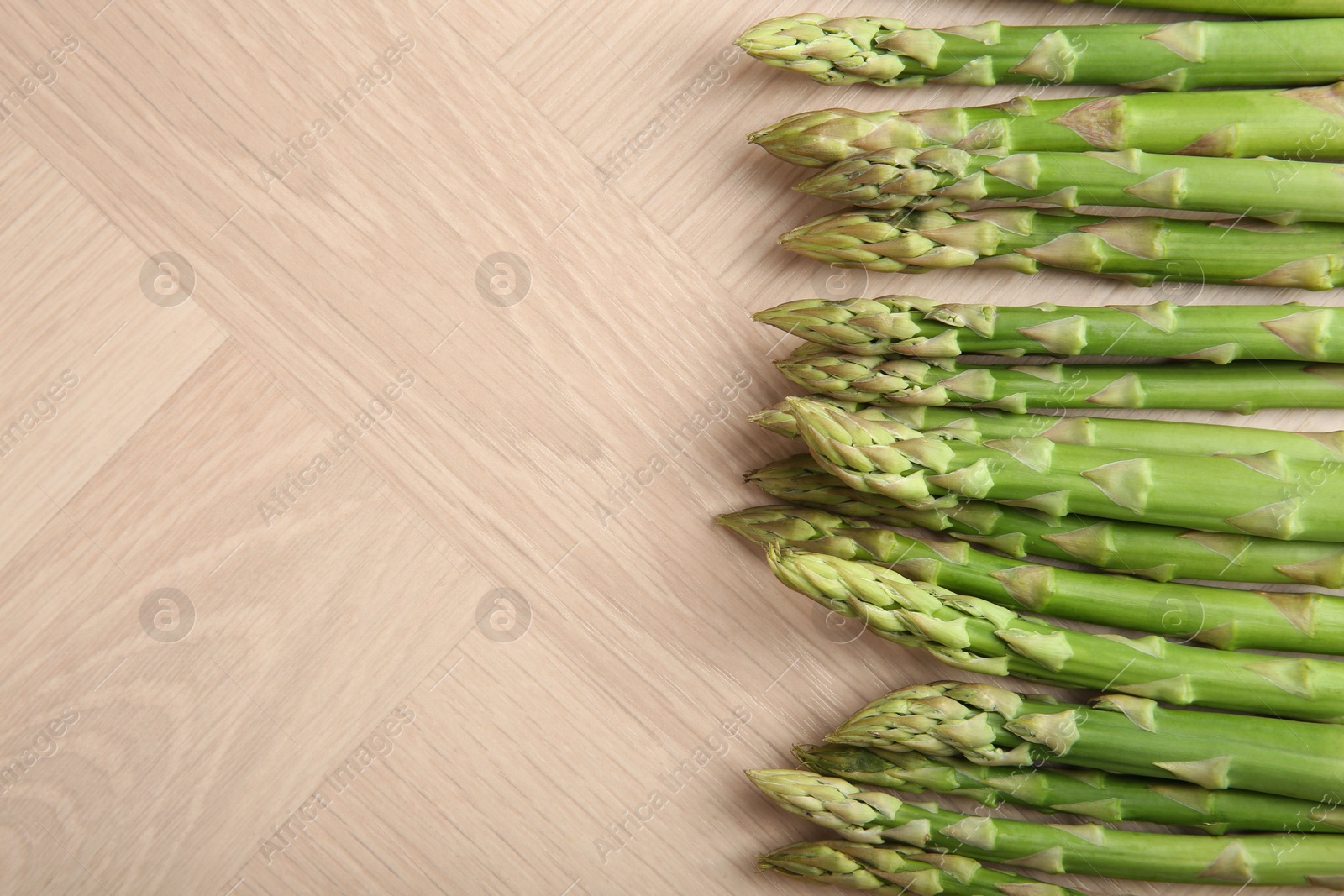 Photo of Fresh green asparagus stems on wooden table, top view. Space for text