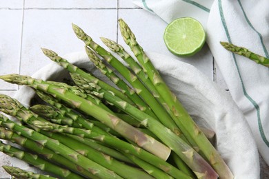 Fresh green asparagus stems and lime on light textured tiled table, flat lay