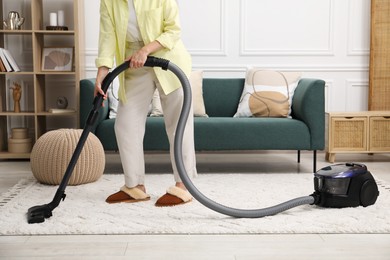 Woman cleaning carpet with vacuum in living room, closeup