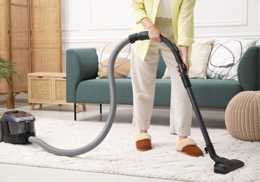 Photo of Woman cleaning carpet with vacuum in living room, closeup