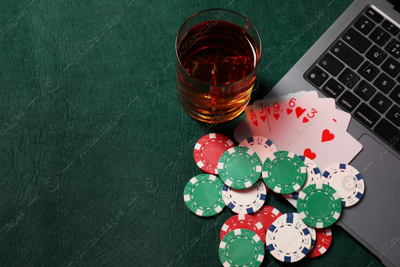 Photo of Poker chips, laptop, playing cards and glass of alcohol drink on green table, flat lay. Online game