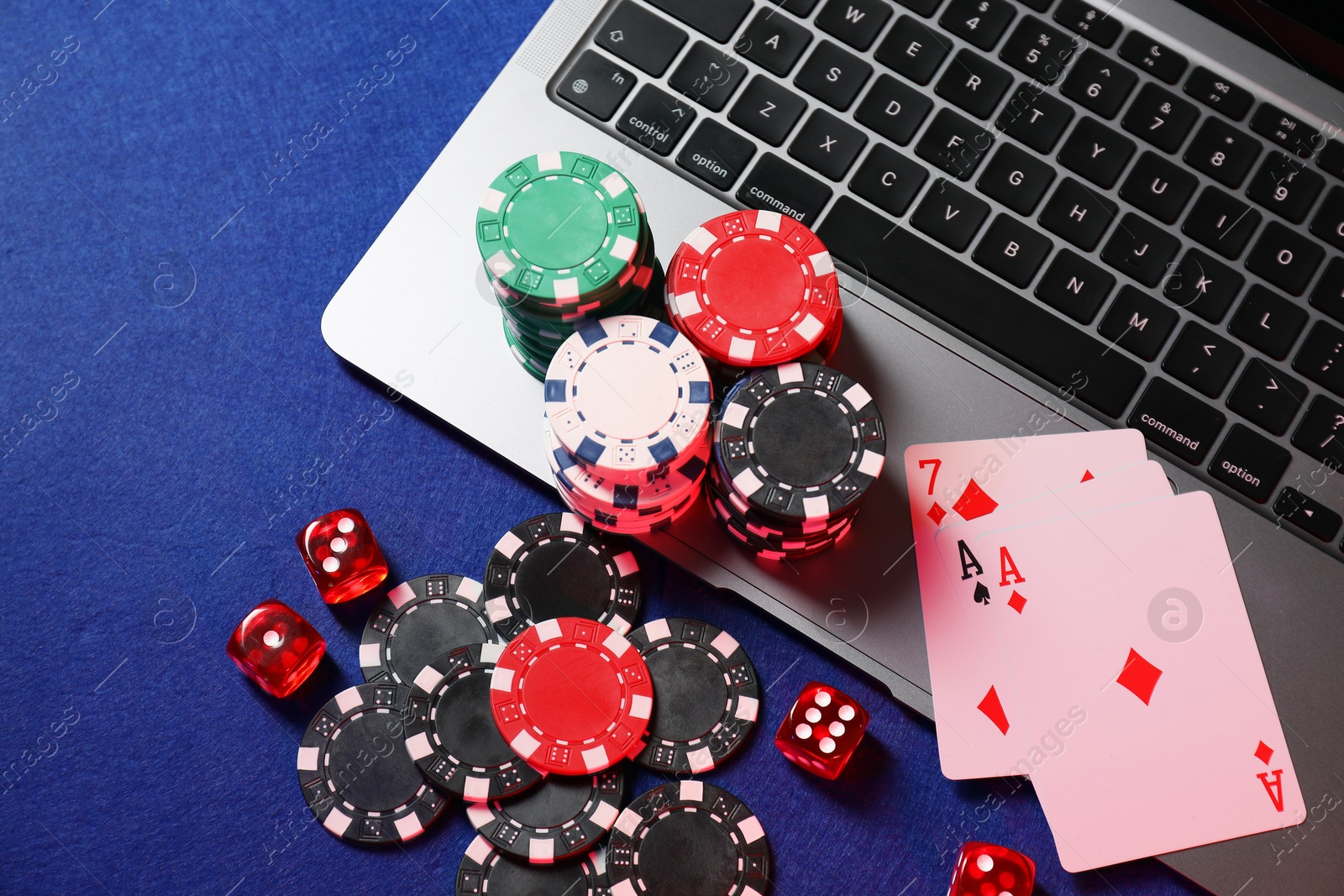 Photo of Poker chips, laptop, playing cards and dices on blue table, flat lay. Online game