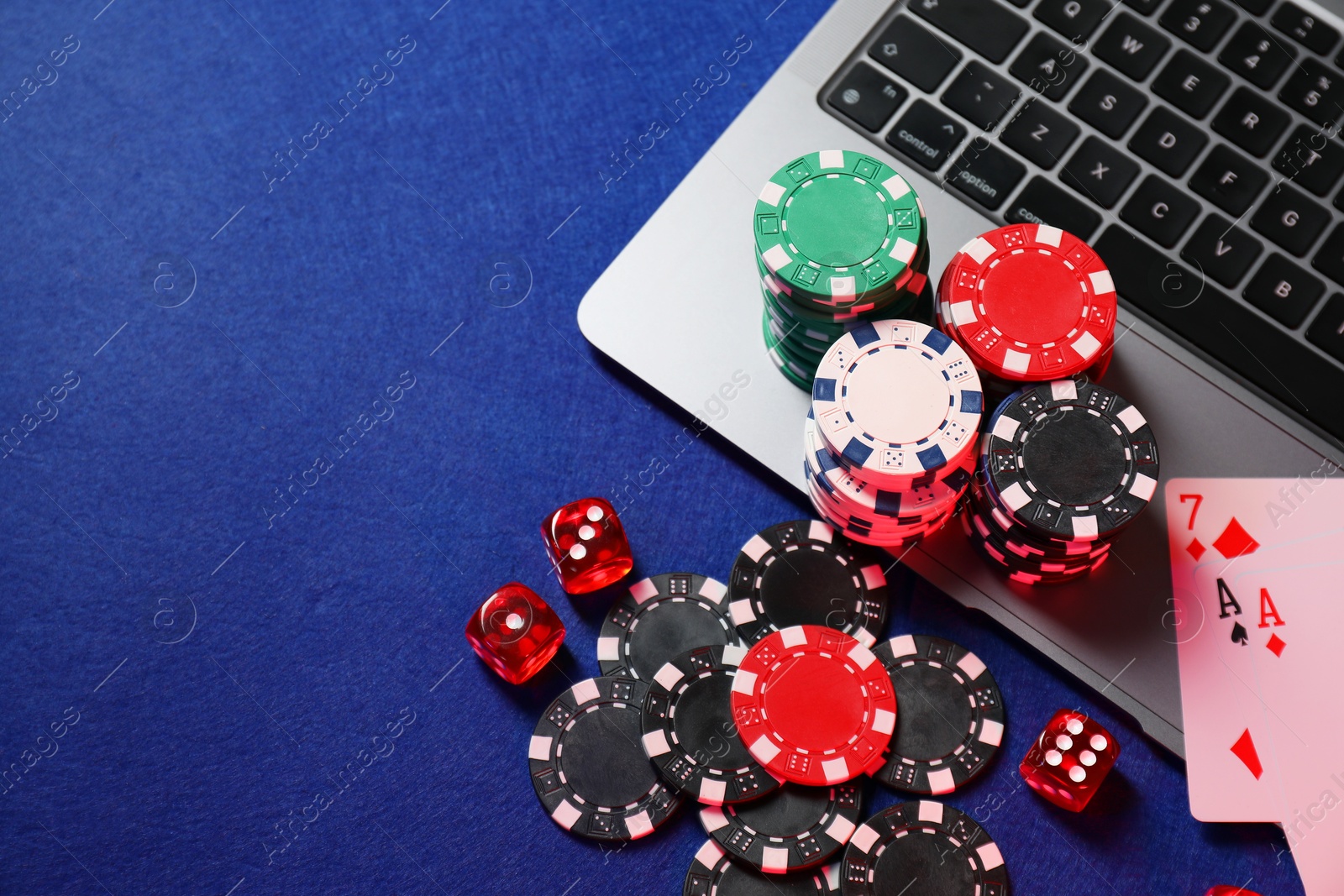 Photo of Online game. Poker chips, laptop, playing cards and dices on blue table, flat lay. Space for text