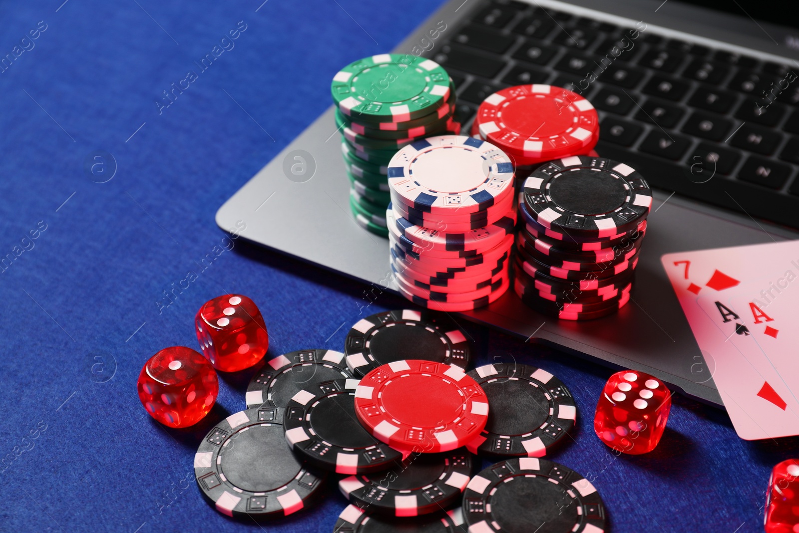 Photo of Poker chips, laptop, playing card and dices on blue table. Online game