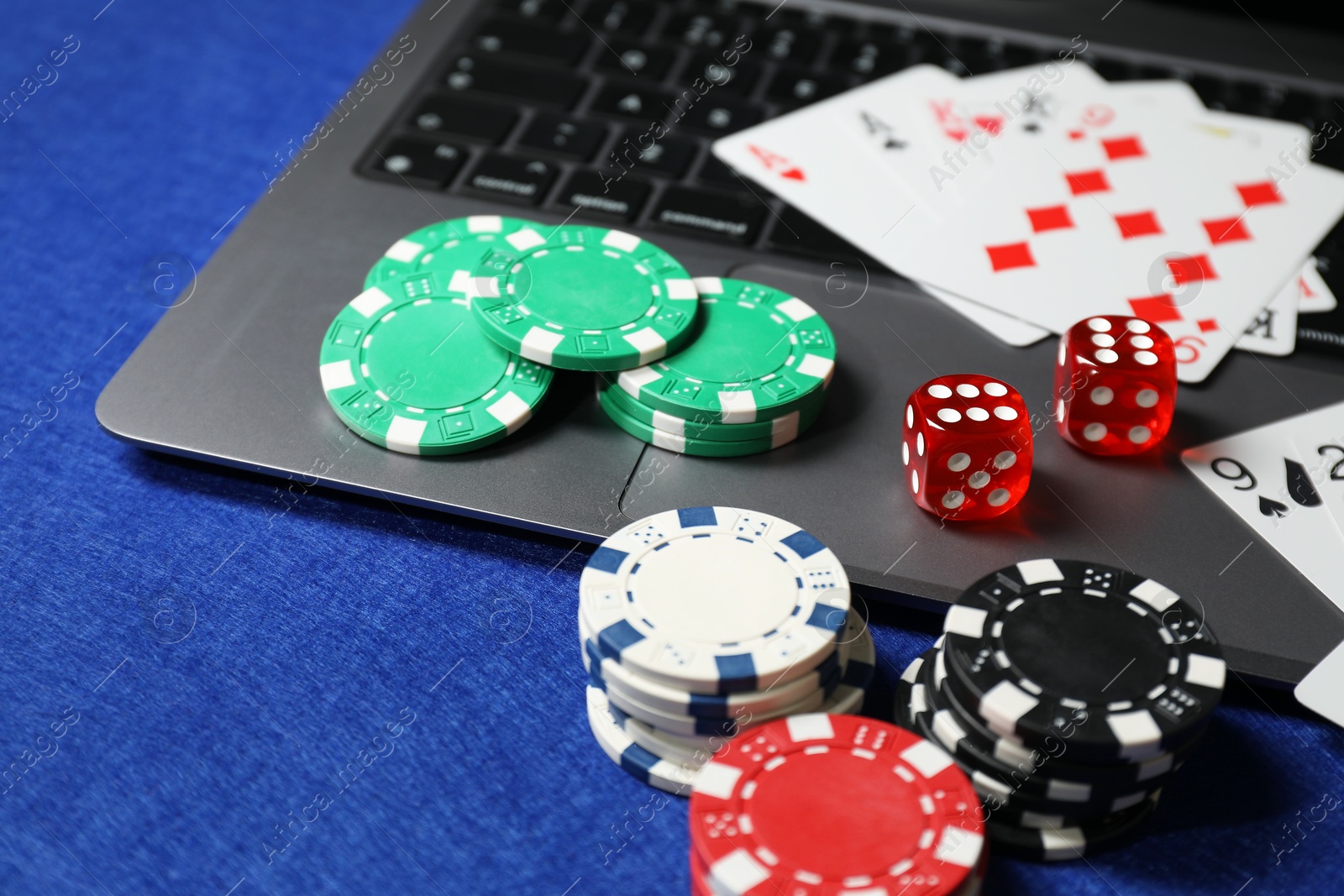 Photo of Poker chips, laptop, playing cards and dices on blue table. Online game