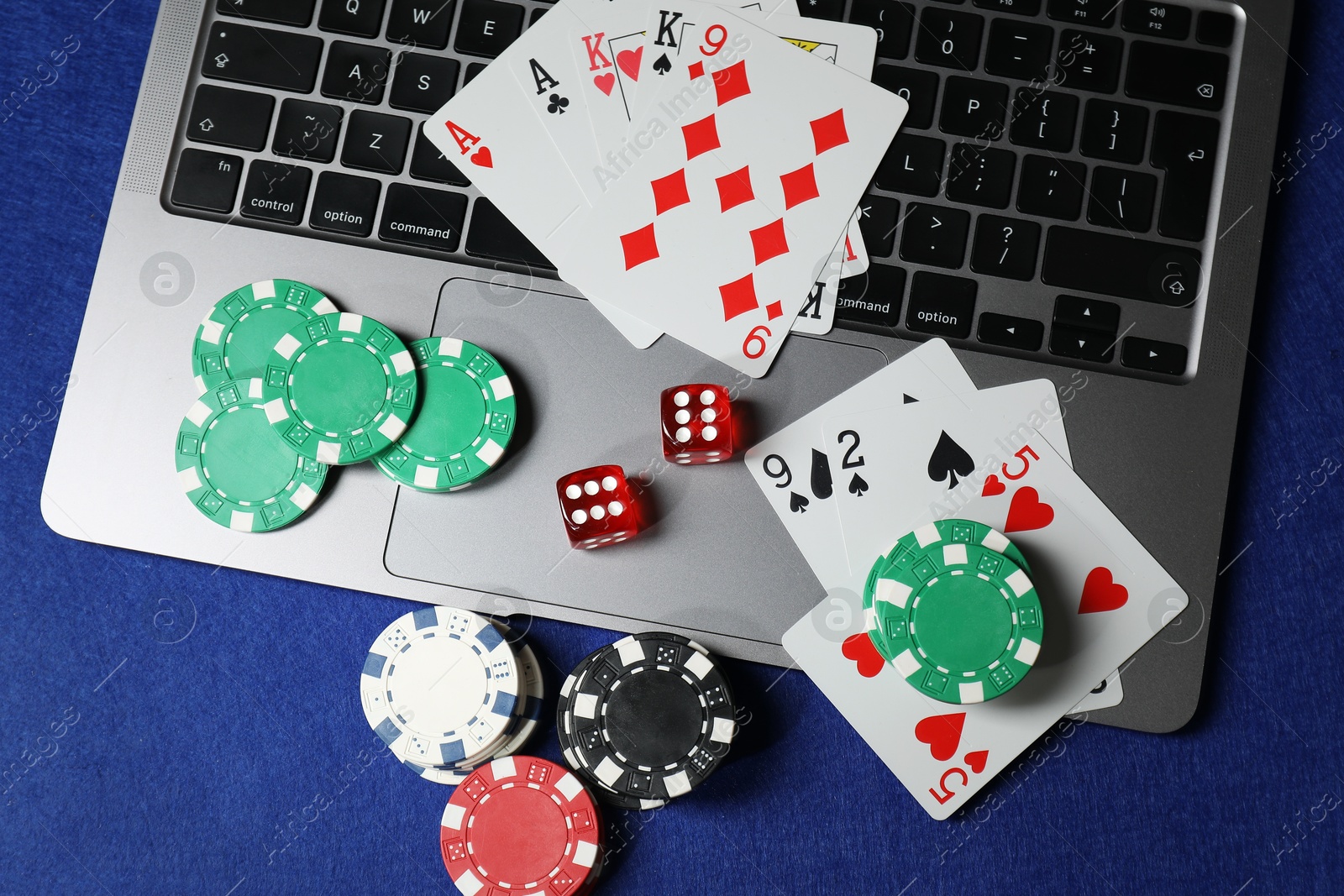 Photo of Poker chips, laptop, playing cards and dices on blue table, flat lay. Online game