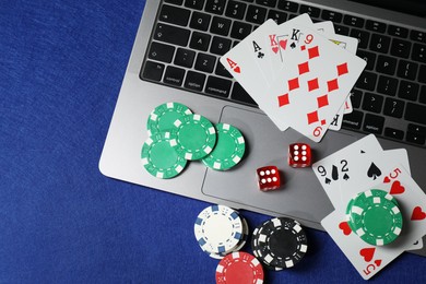 Photo of Poker chips, laptop, playing cards and dices on blue table, flat lay. Online game