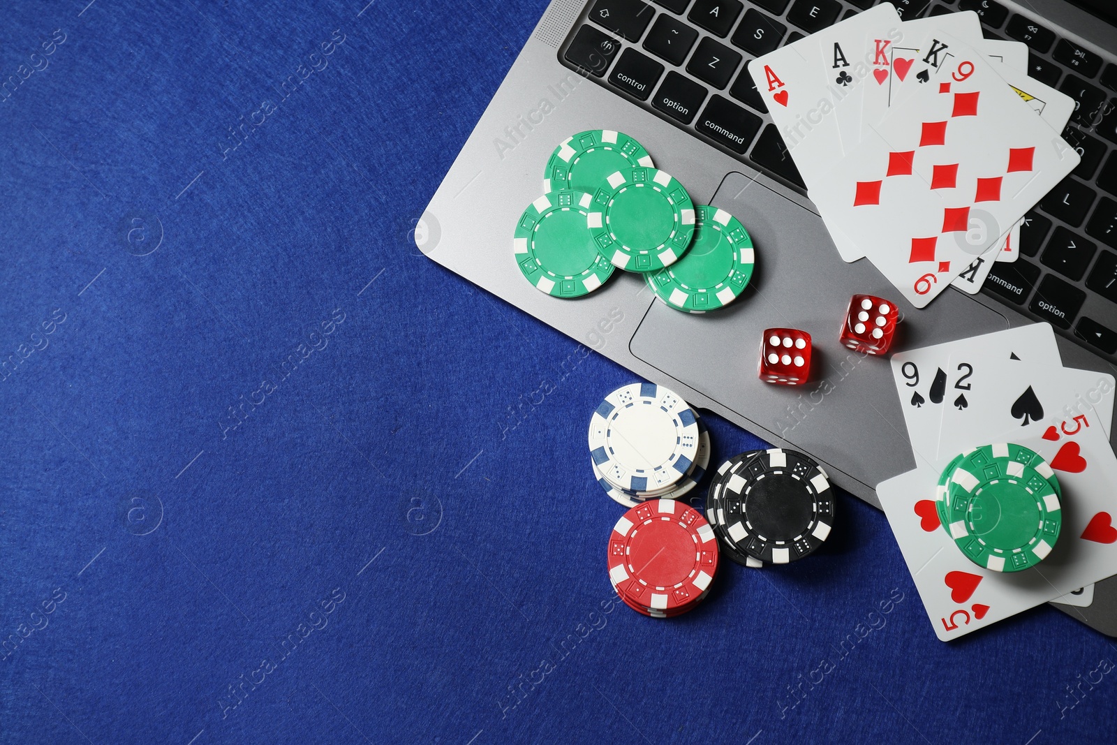 Photo of Online game. Poker chips, laptop, playing cards and dices on blue table, flat lay. Space for text