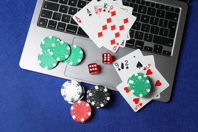 Photo of Poker chips, laptop, playing cards and dices on blue table, flat lay. Online game