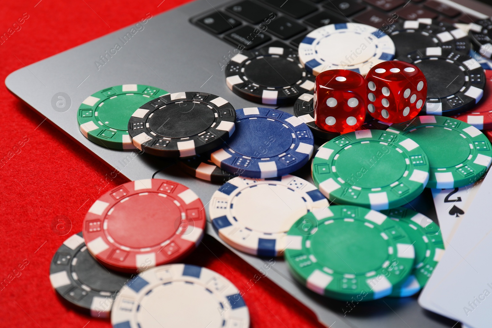 Photo of Poker chips, laptop and dices on red table, closeup. Online game