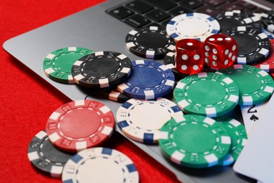 Photo of Poker chips, laptop and dices on red table, closeup. Online game