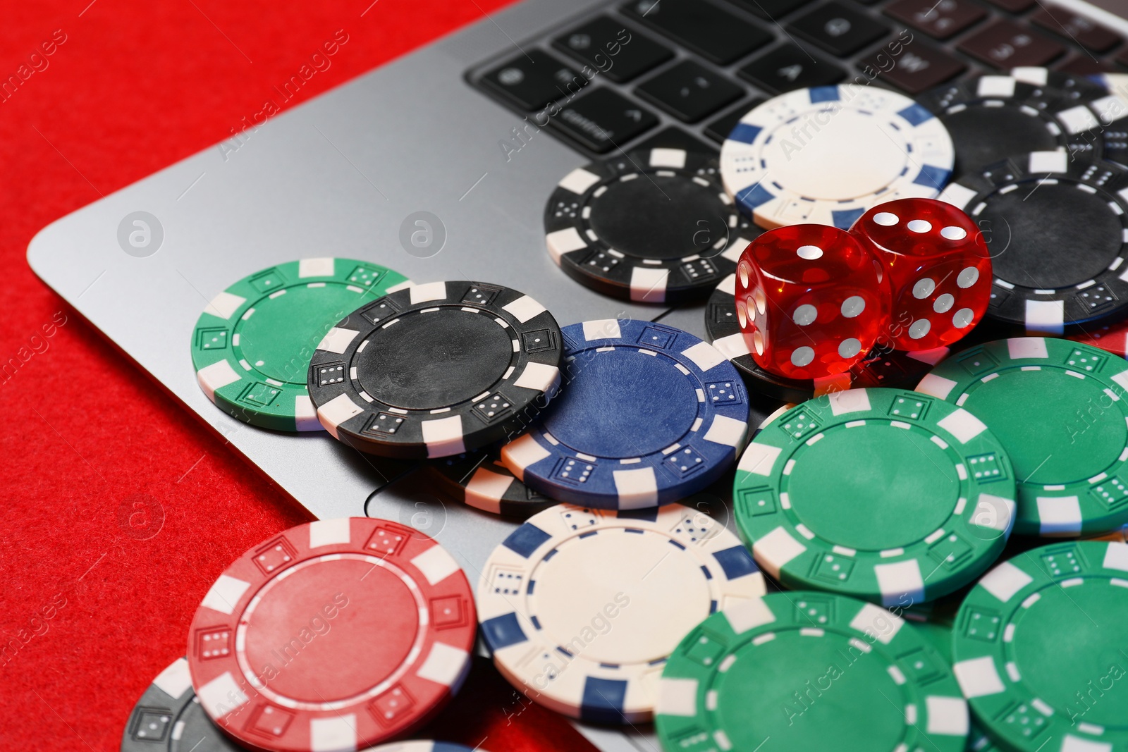 Photo of Poker chips, laptop and dices on red table, closeup. Online game