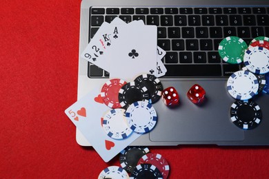 Photo of Poker chips, laptop, playing cards and dices on red table, flat lay. Online game