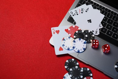 Photo of Online game. Poker chips, laptop, playing cards and dices on red table, flat lay. Space for text