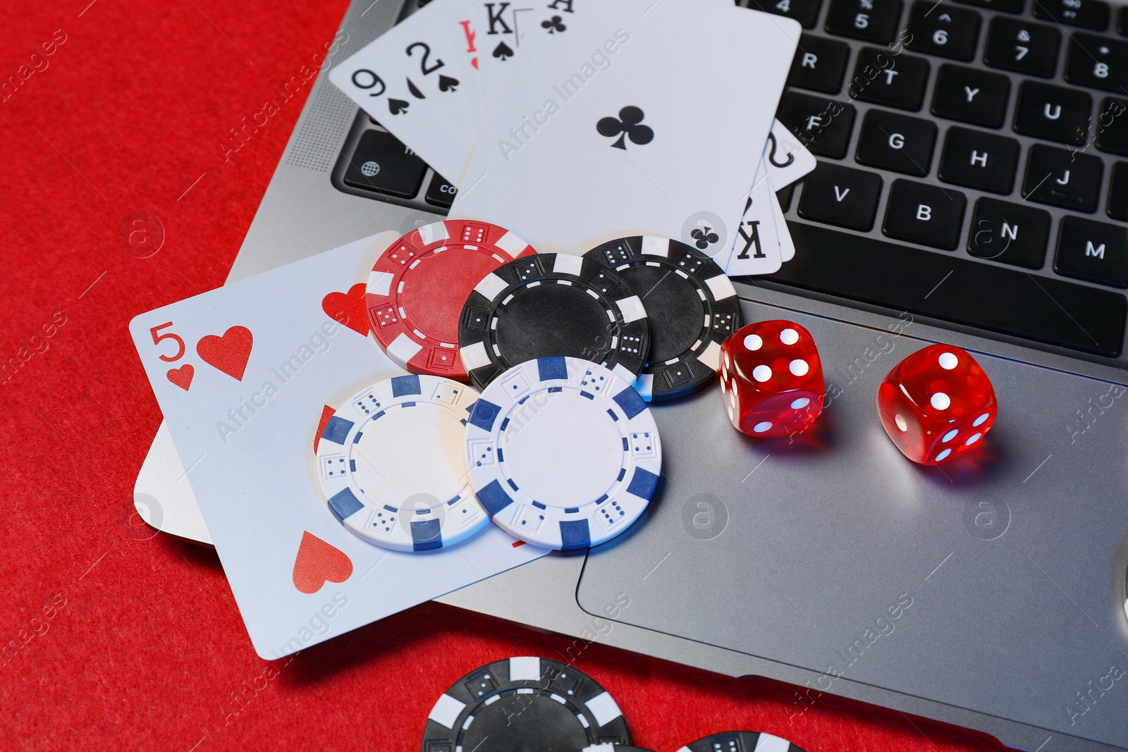 Photo of Poker chips, laptop, playing cards and dices on red table. Online game