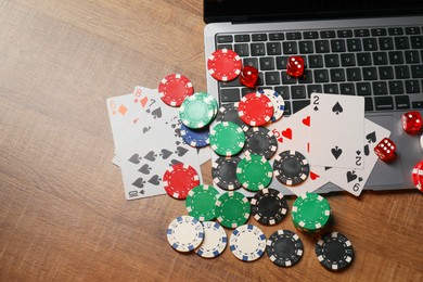 Photo of Poker chips, laptop, playing cards and dices on wooden table, flat lay. Online game