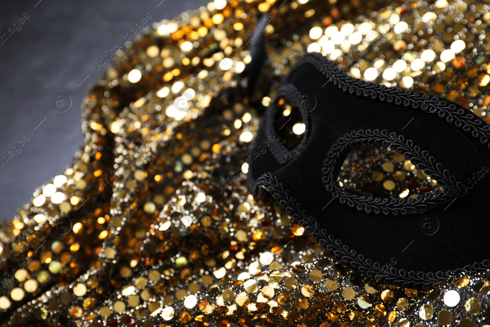 Photo of Beautiful carnival mask and fabric with golden sequins on grey table, closeup