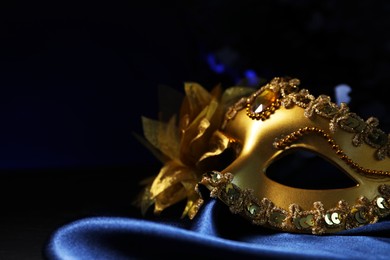 Photo of Beautiful golden carnival mask on blue fabric in darkness, closeup