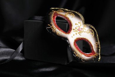 Photo of Beautiful carnival mask on black silk fabric, closeup