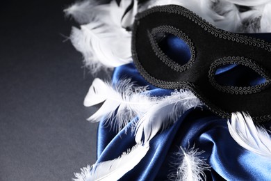 Beautiful carnival mask, white feathers and blue silk fabric on black background, closeup