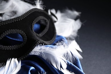 Beautiful carnival mask, white feathers and blue silk fabric on black background, closeup