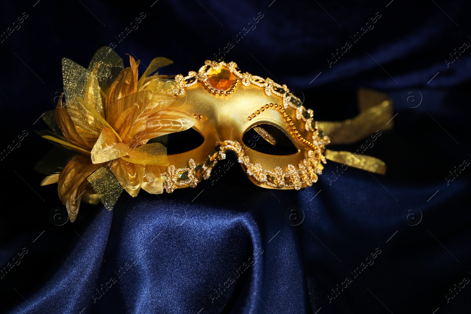 Photo of Beautiful golden carnival mask on blue silk fabric, closeup