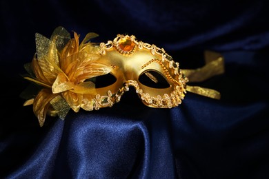 Photo of Beautiful golden carnival mask on blue silk fabric, closeup