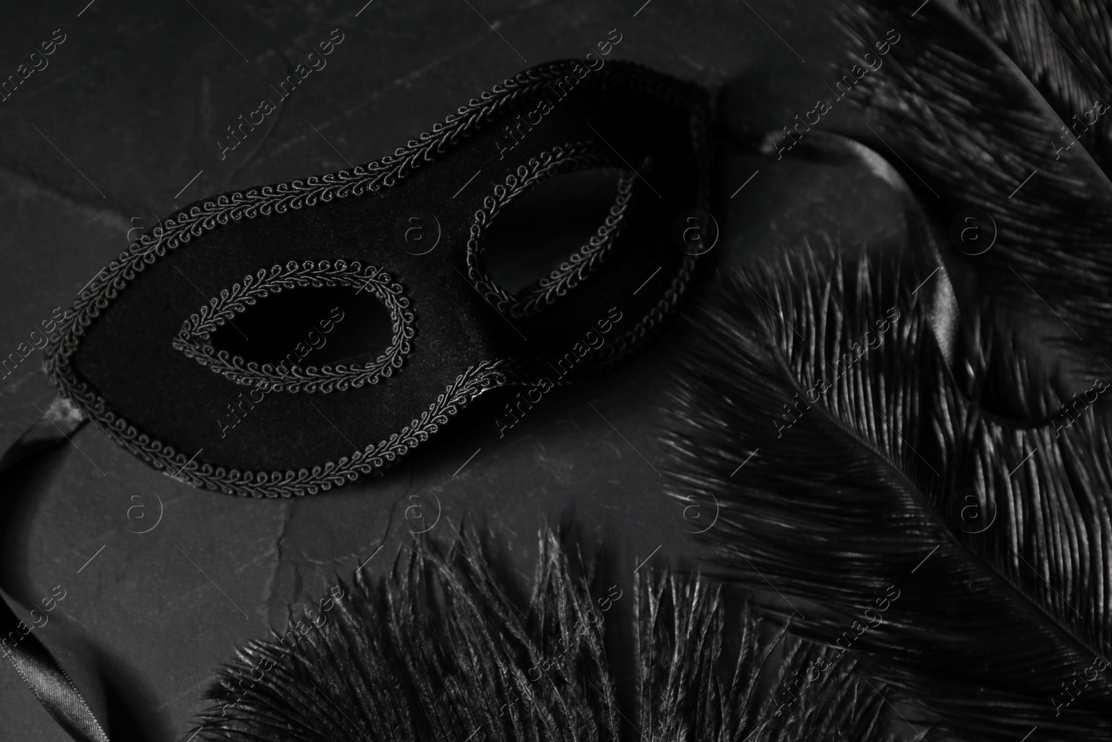 Photo of Beautiful carnival mask and feathers on black table, closeup