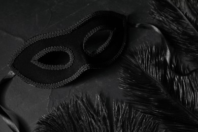 Photo of Beautiful carnival mask and feathers on black table, closeup