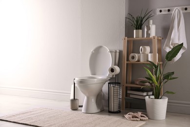 Photo of White toilet bowl, paper rolls and houseplants in bathroom, space for text