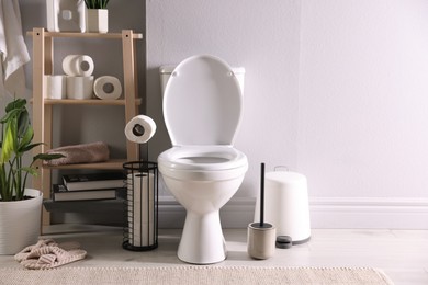 Photo of White toilet bowl, paper rolls and houseplant in bathroom