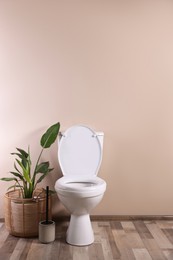 Photo of White toilet bowl and houseplant near beige wall indoors. Space for text